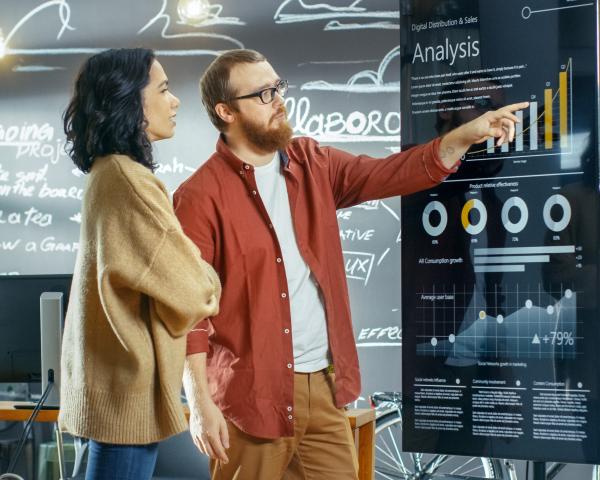 Female Developer and Male Statistician Use Interactive Whiteboard Presentation Touchscreen to Look at Charts, Graphs and Growth Statistics. They Work in the Stylish Creative Office.